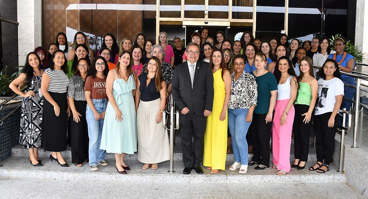 A imagem mostra um grande grupo de mulheres reunidas em frente a um prédio. São servidoras, cola...