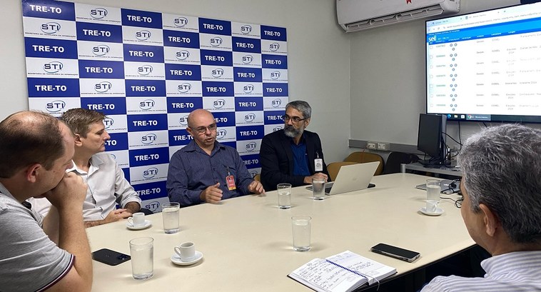 A imagem mostra uma reunião em uma sala de conferências. Seis homens estão sentados ao redor de ...